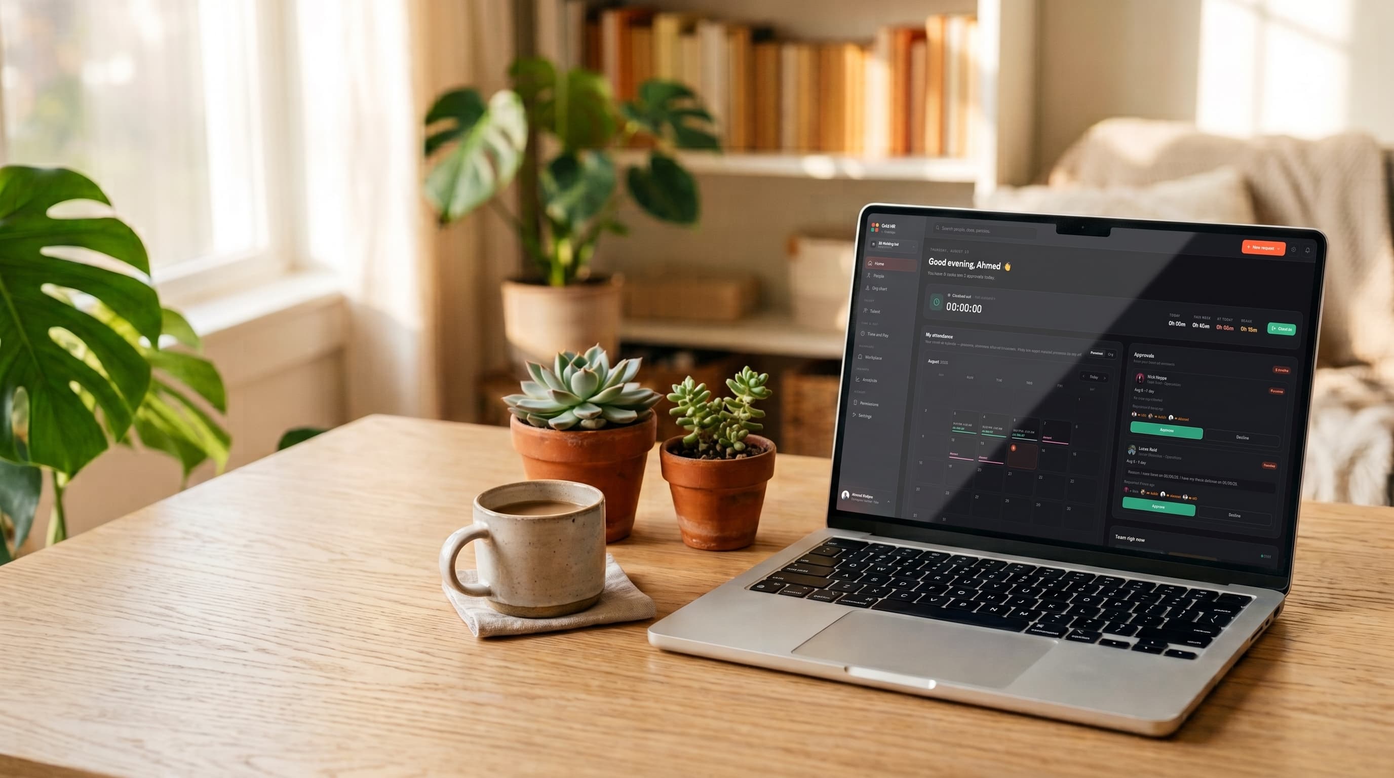 The Grid HR dashboard — attendance calendar, time-off approvals and team celebrations — open on a laptop on a sunlit desk beside a coffee and two succulents.